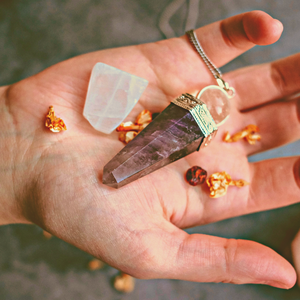 pendules en pierre taillée amethyste sur monture métal argenté dans une main de femme avec quartz blanc art divinatoire
